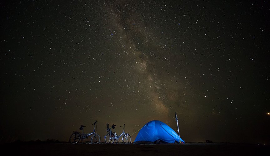 Tent of cycling tourists against the background of the night sky in the village of Portovoye